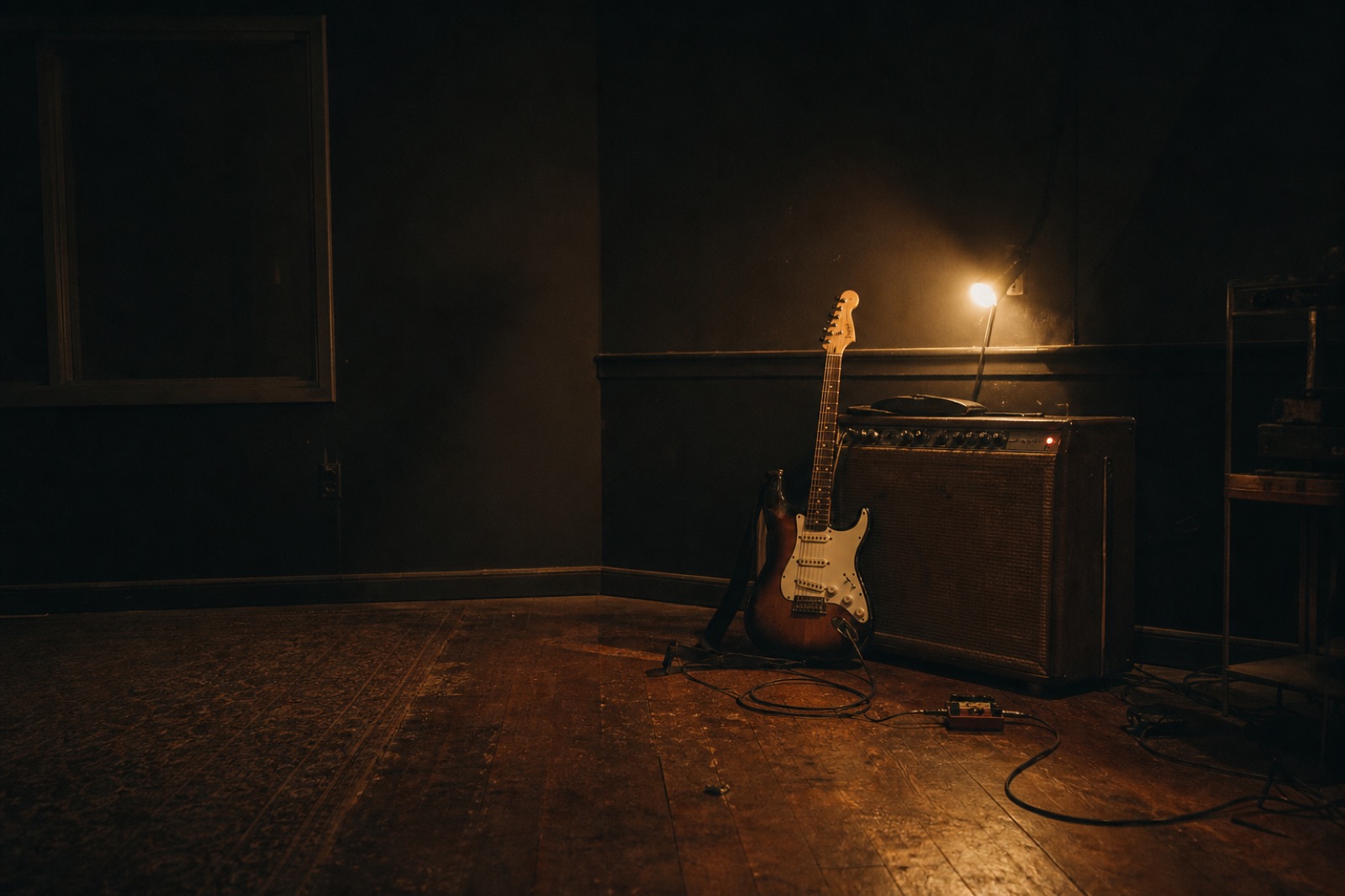 Electric guitar beside a valve amplifier in a dim rehearsal room