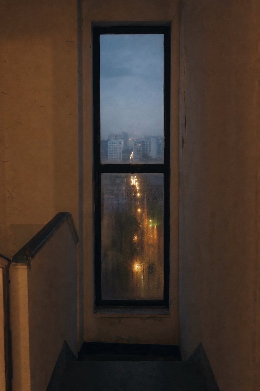 Tall stairwell window looking toward the city at dusk