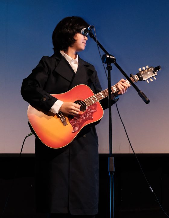 Yuhe on stage, singing and playing an acoustic guitar.